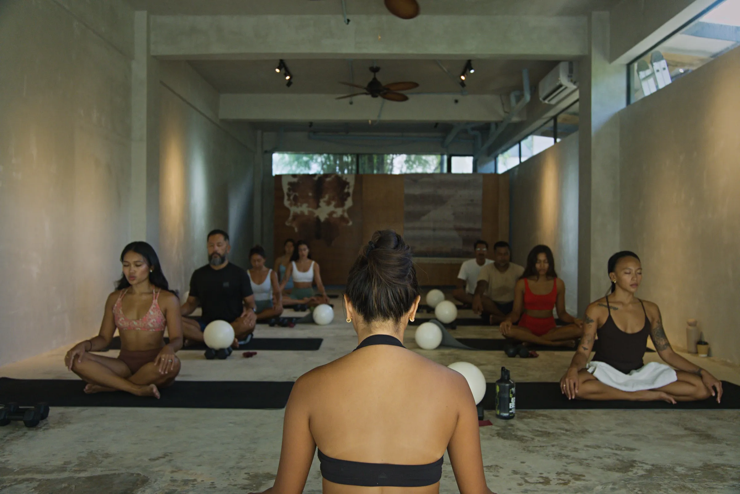 A group class seated together in a circle on the studio floor at Feral Studio in Malinao, General Luna, Siargao, the instructor leading a moment of stillness