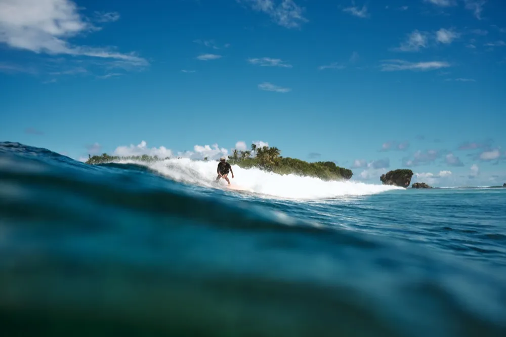 Surfer riding a wave with palm-covered island in the background — Siargao surf adventure