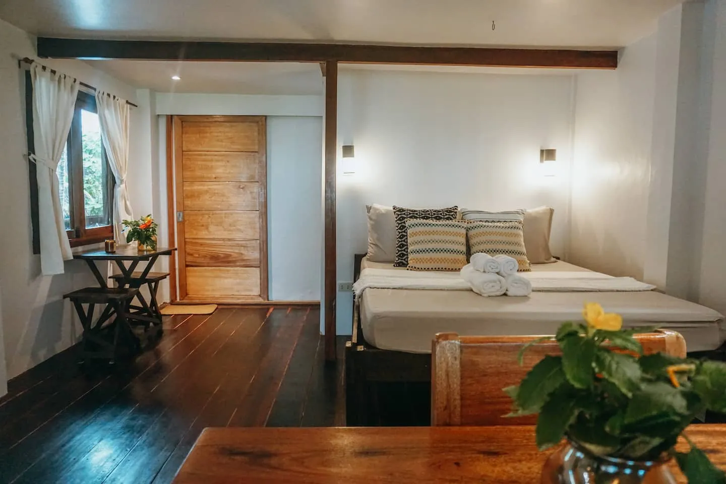 A warm wood bedroom with layered cushions opening onto the deck at Vultun House
