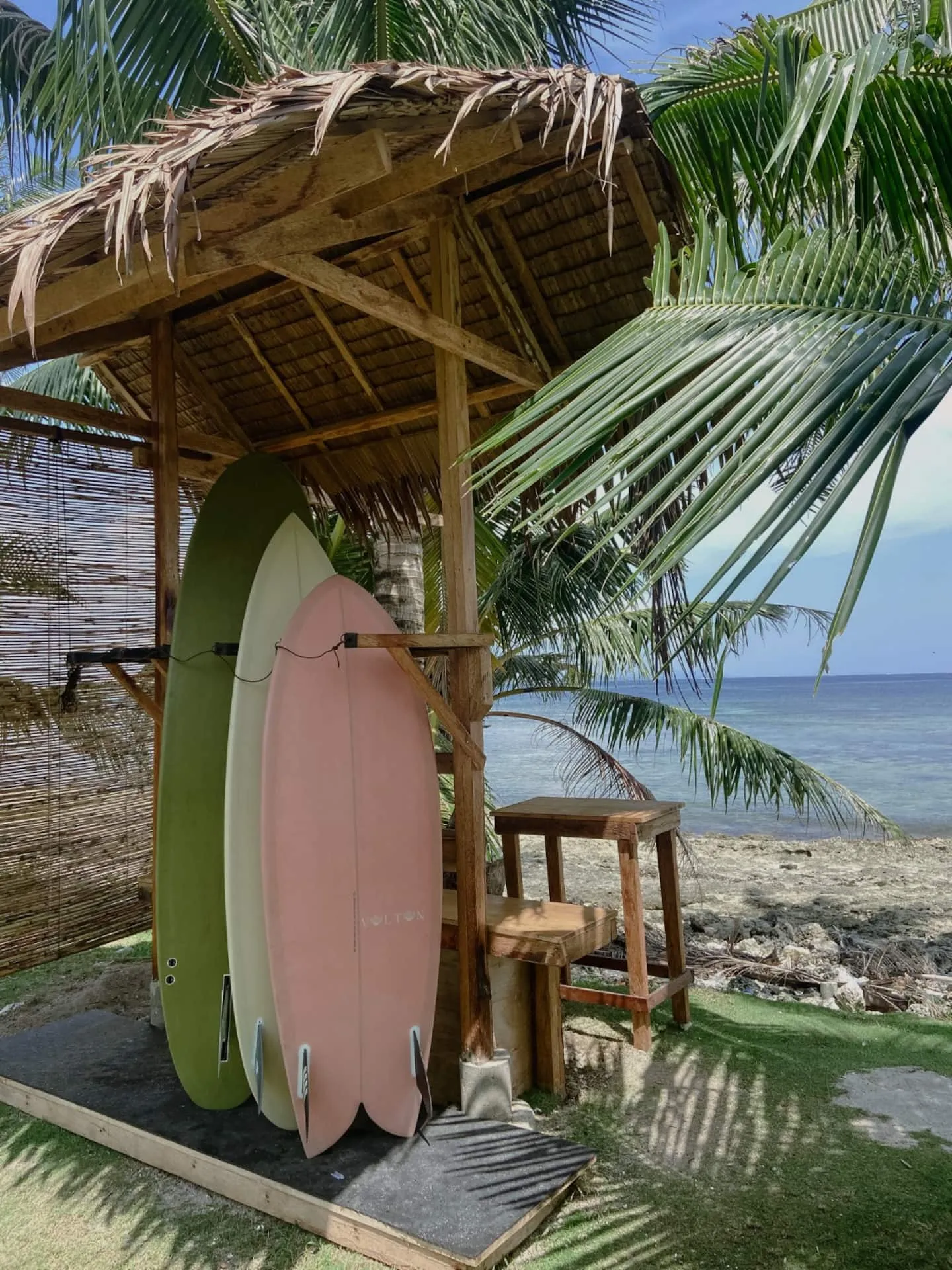 Surfboards on the surf rack beside the deck with palms and the ocean beyond at Vultun House, Siargao
