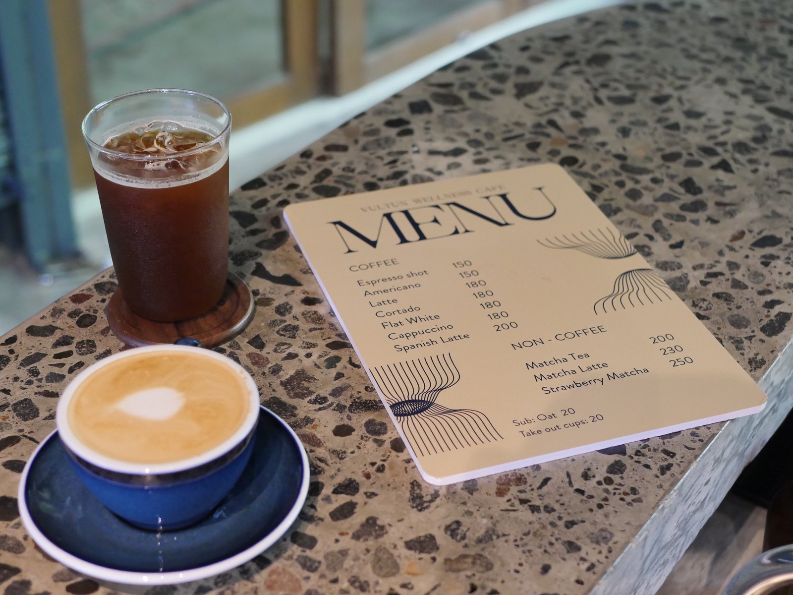 Vultun Wellness Cafe menu card alongside an iced Americano and a flat white in a navy ceramic cup, Siargao