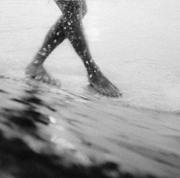 Surfer walking through shallow ocean water in black and white