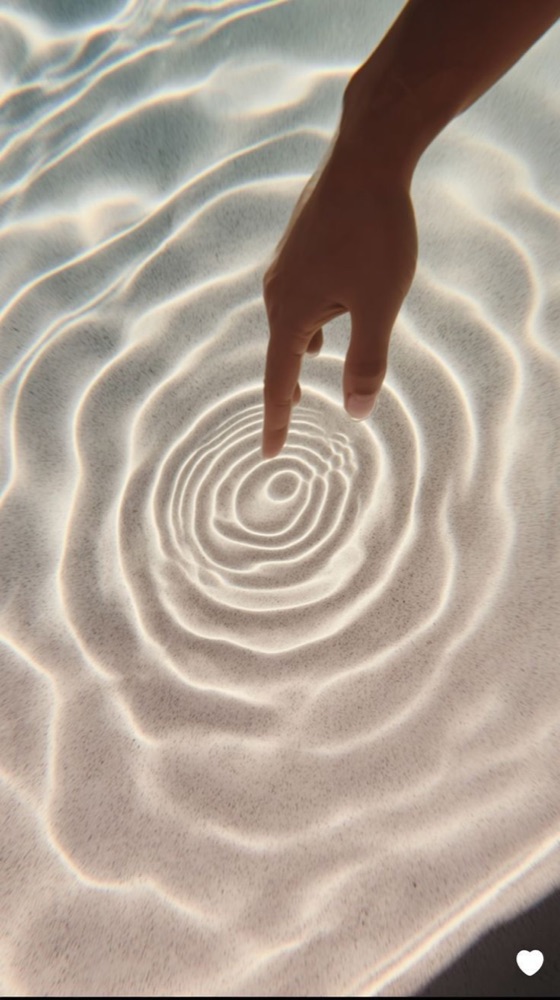 Hand touching water creating ripples — stillness and presence